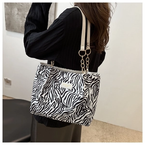 Detail of zebra print tote bag featuring white leather straps and gold metal chain links