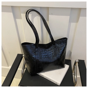 Detail view of the black crocodile pattern texture on a shiny patent leather tote bag