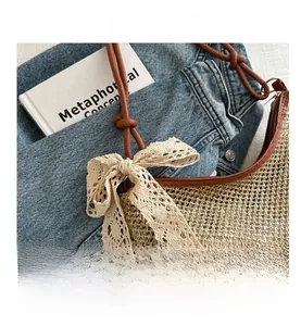 Detailed close-up of woven straw bag with beige lace bow and brown leather shoulder strap
