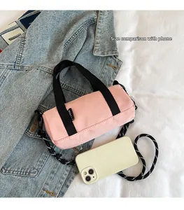 Sac cylindrique rose avec bandoulière rayée placé à côté d'un smartphone pour comparer la taille