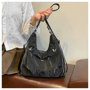 Detail of black pleated tote bag with silver butterfly charms and glossy texture