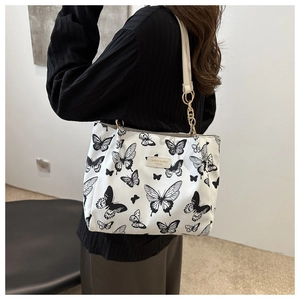 Detail view of white canvas tote bag featuring black butterfly prints and chain strap