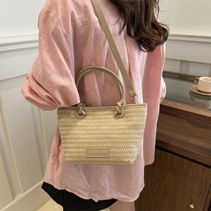 Détail d'un sac cabas en paille tressée avec poignées en cuir et étiquette tendance