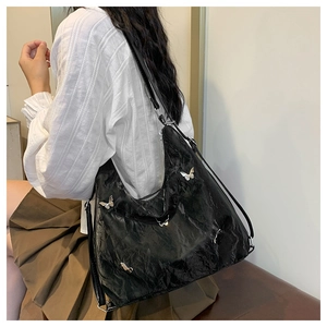 Detail of black textured leather bag with silver butterfly charms on model's shoulder