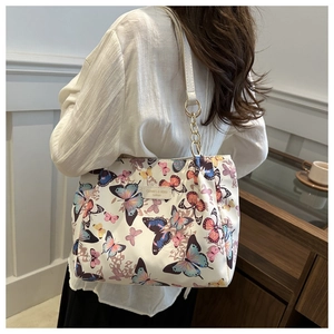 Detail of white canvas tote bag with butterfly print and leather chain strap shown on model