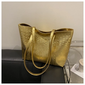 Detail of large gold tote bag with crocodile texture and shoulder straps on a sofa