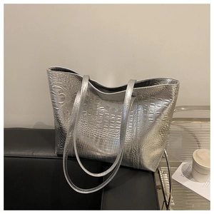 Detail of silver crocodile pattern tote bag with dual straps on a black leather sofa