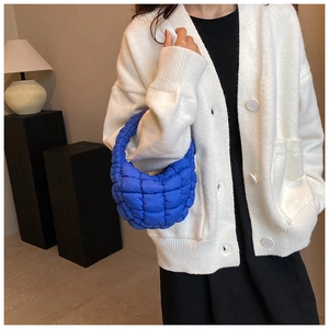 Detail of blue quilted puffer handbag with soft square texture and portable handle