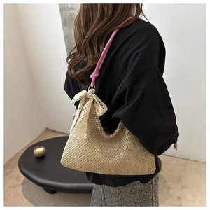 Detail of hand-woven straw bag with pink knot strap and decorative lace bow