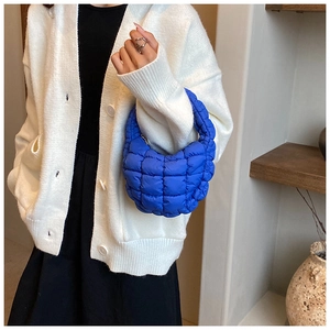 Close-up of bright blue quilted cloud handbag styled with a white knit cardigan