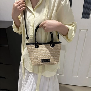 Détail de la texture tressée beige avec poignées en cuir noir et logo sur le sac cabas