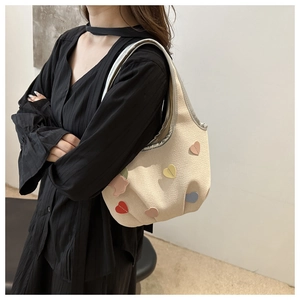 Détail d'un sac sous les bras beige avec écussons cœurs colorés et design plissé texturé