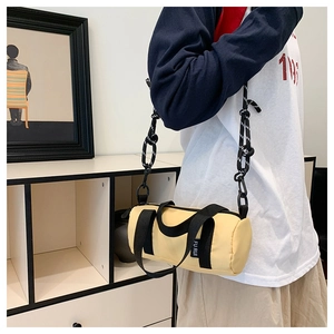 Détail d'un sac bandoulière cylindrique jaune vif avec des lanières noires nouées et anse