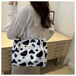 Detail of canvas tote bag with cow print pattern and gold chain strap on a model