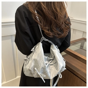 Detail of silver metallic pleated shoulder bag with decorative bow ties and zipper