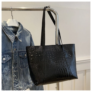 Detail of glossy black crocodile embossed tote bag hanging on a rack with denim jacket
