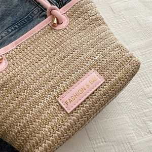 Gros plan du sac cabas en paille tressée avec garniture en cuir rose et logo doré