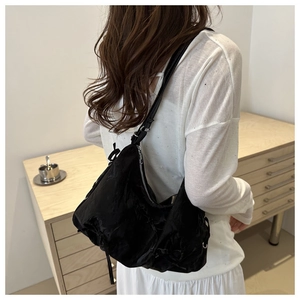 Detail of black pleated shoulder bag with decorative ribbons and glossy finish texture