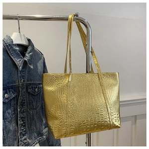 Macro shot of metallic gold tote bag with crocodile texture hanging on a silver rack