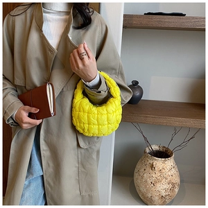 Detail of a bright yellow quilted bubble bag held by a model in a minimalist setting