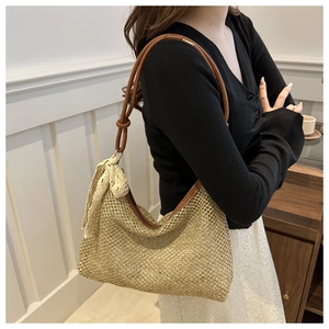 Detail of woven straw shoulder bag featuring a brown leather strap and lace bow charm