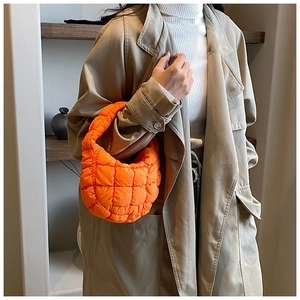 Detail of bright orange quilted puffy handbag worn over a neutral trench coat