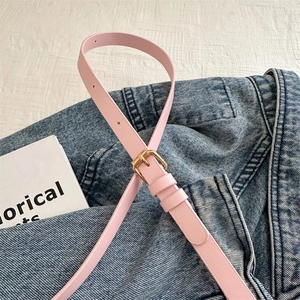 Détail d'une ceinture fine en cuir rose avec boucle dorée sur une veste en jean