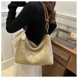 Detail of woven straw shoulder bag with brown leather strap and delicate lace bow