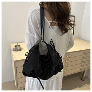 Rear view of black pleated shoulder bag with bow details on a model in a minimal room