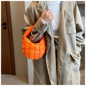 Detail of a bright orange quilted puffer handbag showing the texture and half-moon design