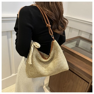 Detail of woven straw bag with brown leather strap, knotted design and lace bow accent