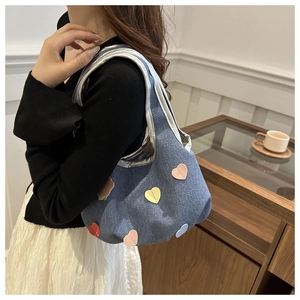 Détail du sac cabas en denim bleu avec écussons en forme de cœur et bordures métallisées