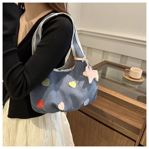 Gros plan d'un sac d'épaule en jean bleu avec patchs de cœurs colorés et petit pendentif