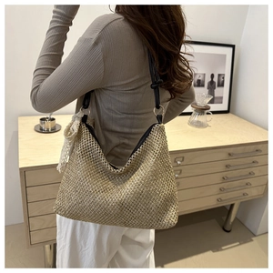 Detail of woven straw tote bag with black leather straps and white lace tassel detail