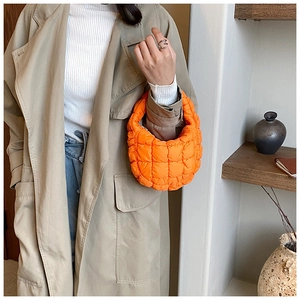 Model wearing a bright orange quilted bubble bag in a stylish minimalist setting