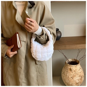 Close-up of a white quilted crescent cloud bag held by a model in a trench coat
