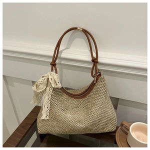 Close-up of woven mesh straw bag with brown leather strap and beige lace bow charm
