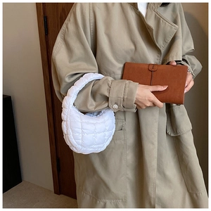 Detailed view of a white quilted dumpling bag carried by a model in a trench coat