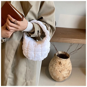 Detail view of a white quilted cloud handbag held by a woman in elegant urban outfit