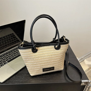 Sac fourre-tout en paille tissée avec poignées en cuir noir et bandoulière sur bureau