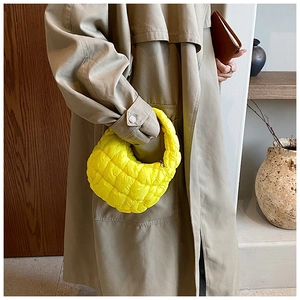 Quilted yellow cloud handbag styled with a beige coat in a minimalist interior setting
