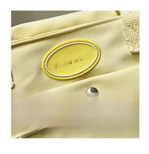 Close-up of yellow fabric tote bag showing silver metal snap button and Fashion label