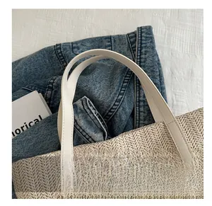 Détail de la texture tressée du sac cabas en paille avec poignée en cuir blanc et couture