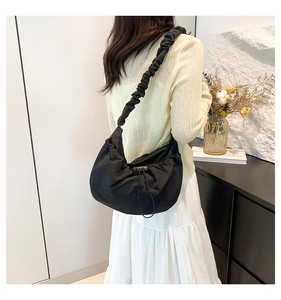 Detail of black nylon crescent shoulder bag with drawstring closure on female model