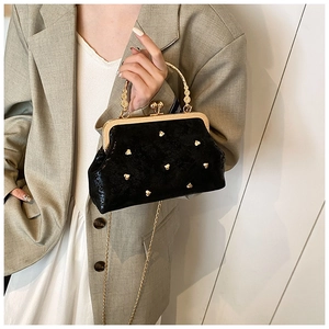 Detail of black velvet evening bag featuring heart rivets and gold chain on model