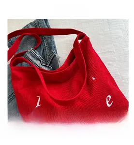 Detail showing the red corduroy fabric texture and white embroidered letters on the tote bag