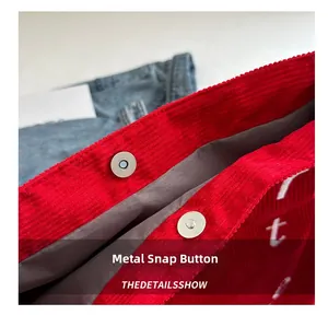 Detailed view of the metal magnetic buckle and white letter print on a red corduroy tote bag