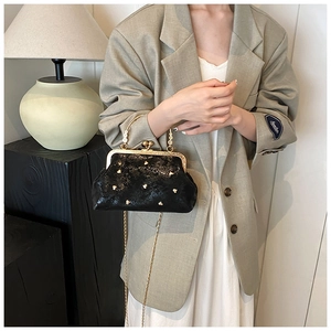 Detail of black glossy frame bag with heart-shaped gold studs and chain strap