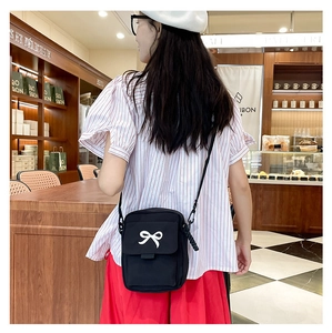 Detail of a black fabric crossbody bag featuring a white bow accent and slim strap