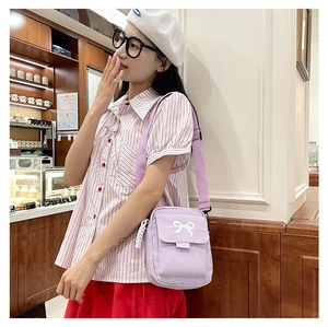 Detail of light purple canvas crossbody bag featuring white bow embroidery and strap